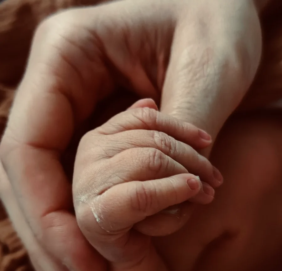 Eine Babyhand umschließt den Finger eines Erwachsenen.